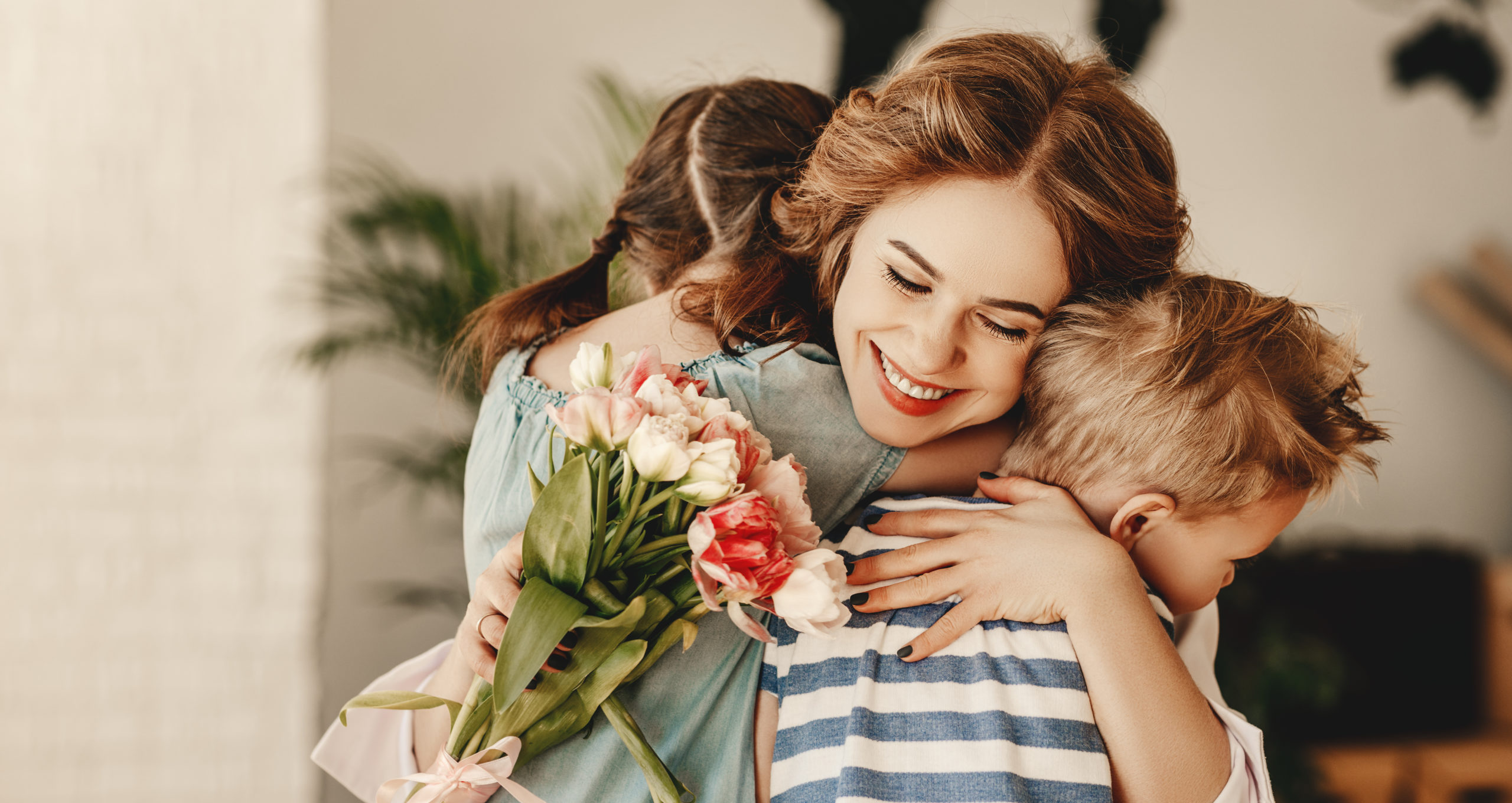 Little children congratulating and hug mother in kitchen